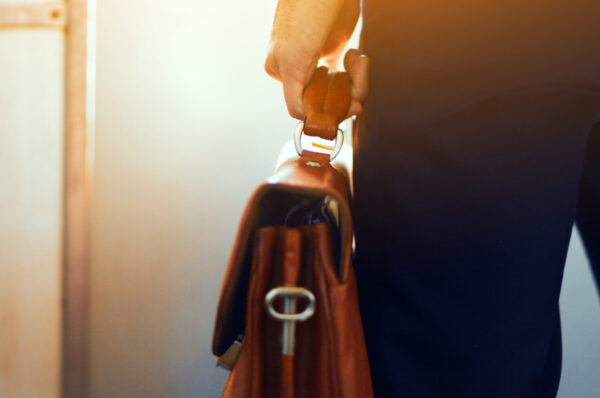 Man holding leather bag while on train. Brown leather case in hands of man. Cropped picture of businessman in suit standing in subway train and holding brown bag in his hand.
