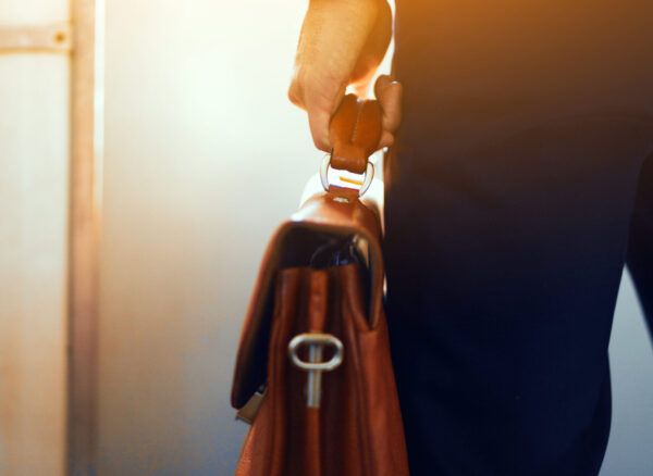 Brown leather case in hands of man. Cropped picture of businessman in suit standing in subway train and holding brown bag in his hand.