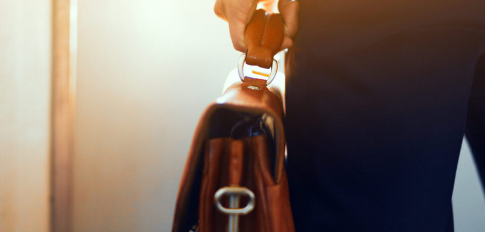 Brown leather case in hands of man. Cropped picture of businessman in suit standing in subway train and holding brown bag in his hand.